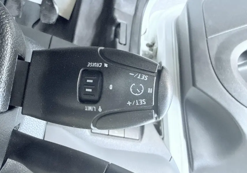 Gros plan sur le commodo de régulateur de vitesse du Peugeot Partner blanc 2014, côté gauche du poste de conduite.