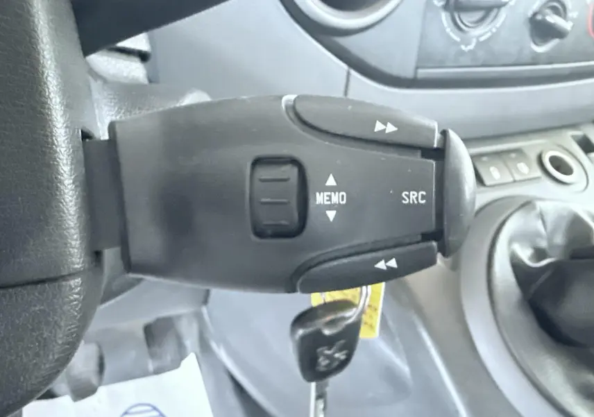 Gros plan sur la commande au volant du Peugeot Partner blanc 2014, avec levier de vitesses manuel visible en arrière-plan.
