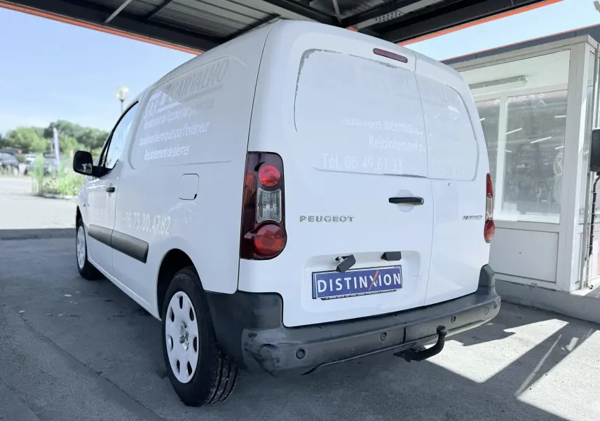 Vue 3/4 arrière droite d’un Peugeot Partner blanc utilitaire avec marquage publicitaire et attelage de remorque.