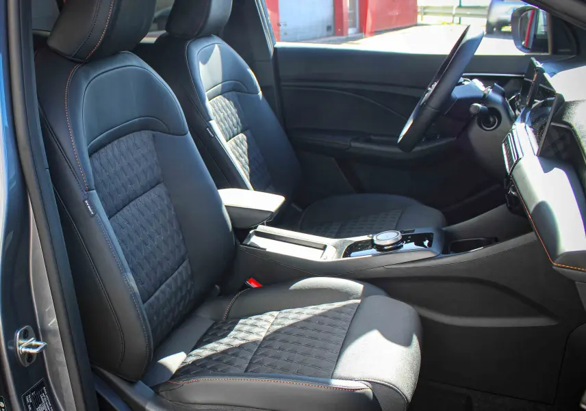 Vue intérieure côté conducteur du MG3 1.5L HYBRID+ 195CH Luxury gris Hampstead, sièges tissu et cuir noirs avec surpiqûres orange.