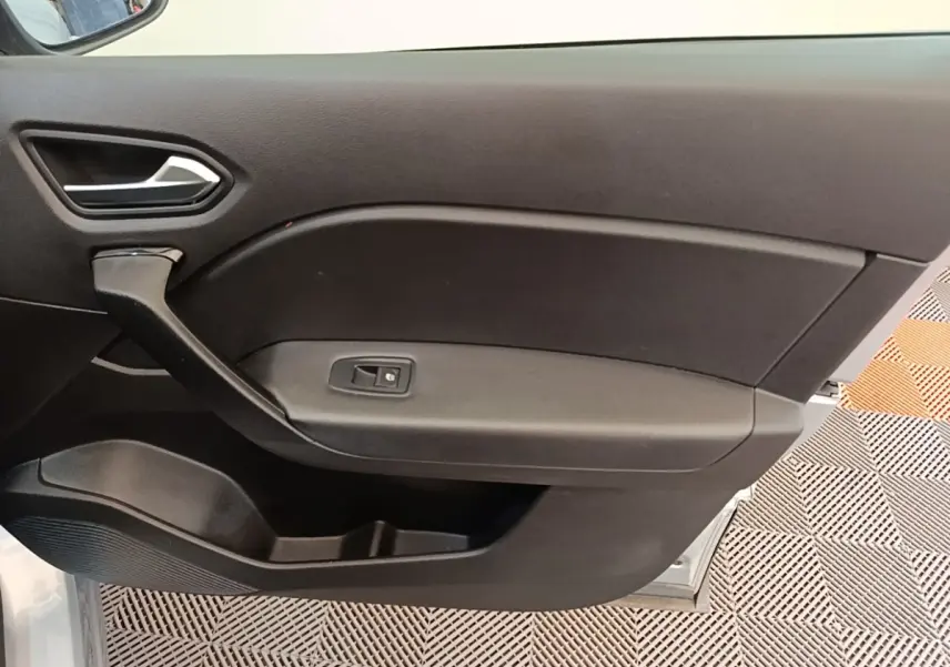 Intérieur côté gauche de la porte avant d’un Renault Captur gris clair, avec poignée et bouton de vitre électrique.