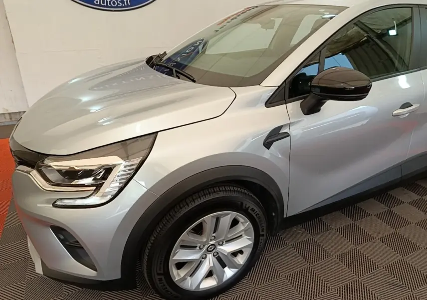 Vue 3/4 avant droit du Renault Captur Business E-Tech hybride gris clair avec jantes alliage et rétroviseur noir brillant.