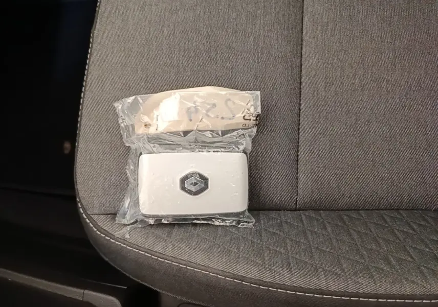 Gros plan sur une clé Renault blanche posée sur un siège tissu gris foncé avec surpiqûres blanches.