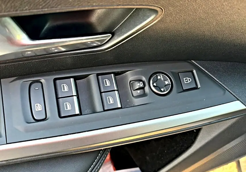 Vue rapprochée des commandes de lève-vitres et rétroviseurs sur la porte côté conducteur d’un Peugeot 3008 gris.