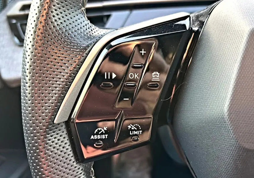 Gros plan sur les commandes noires multifonctions du volant en cuir perforé côté gauche du Peugeot 3008 gris 2025.