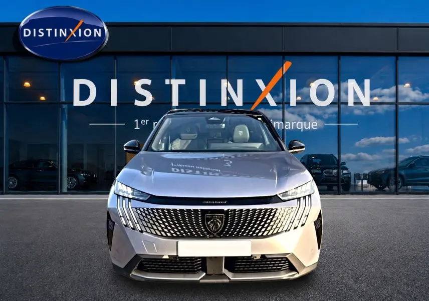 Vue frontale d'un Peugeot 3008 gris 2025 avec calandre distinctive et phares LED fins, devant une vitrine Distinxion.