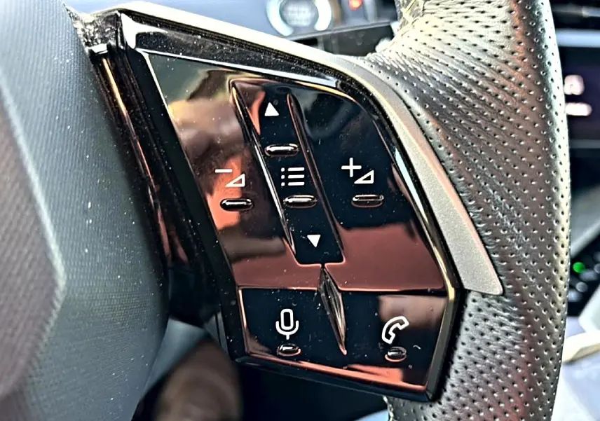 Gros plan sur les commandes vocales et audio noires sur le côté gauche du volant cuir perforé du Peugeot 3008 gris.