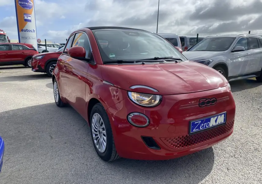 Fiat 500 Cabriolet électrique rouge vue 3/4 avant droit avec phares allumés sur parking extérieur.