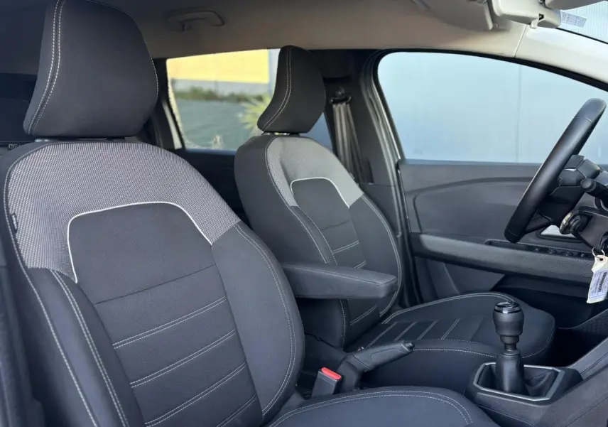 Vue intérieure côté conducteur du Dacia Jogger gris Schiste, mettant en valeur les sièges avant noirs avec accoudoir et la boîte manuelle.