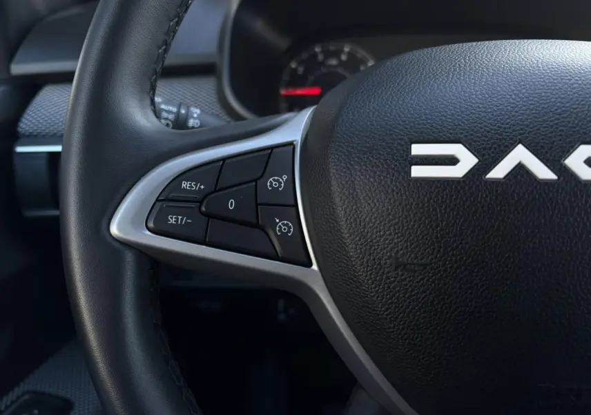 Gros plan sur le volant noir de la Dacia Jogger 2025, montrant les commandes de régulateur de vitesse côté gauche.