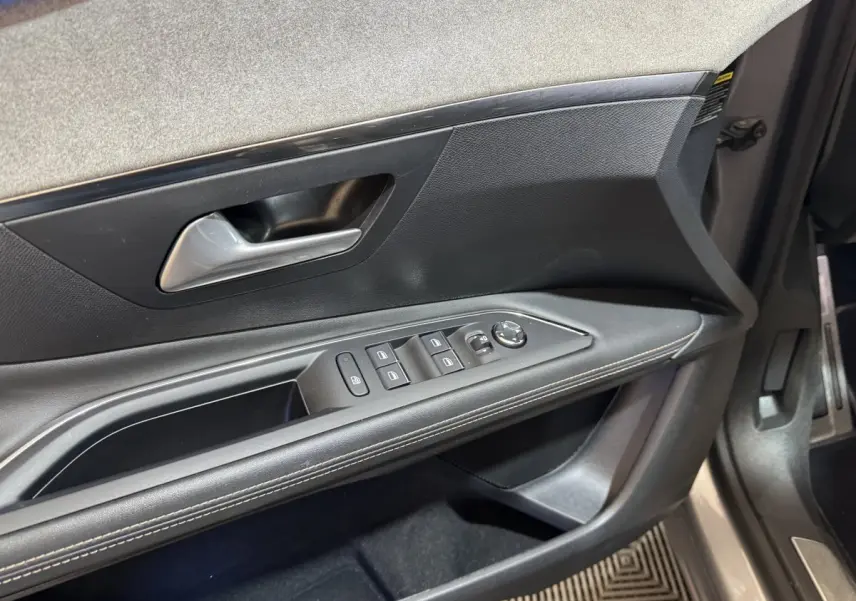 Gros plan sur la porte avant gauche intérieure noire avec commandes des vitres et poignée argentée du Peugeot 3008 gris clair.