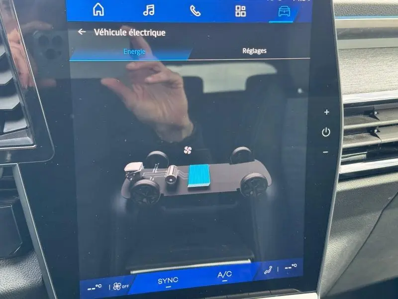 Écran tactile intérieur montrant l'animation du système électrique du Renault Austral 2025, avec reflet de main visible.