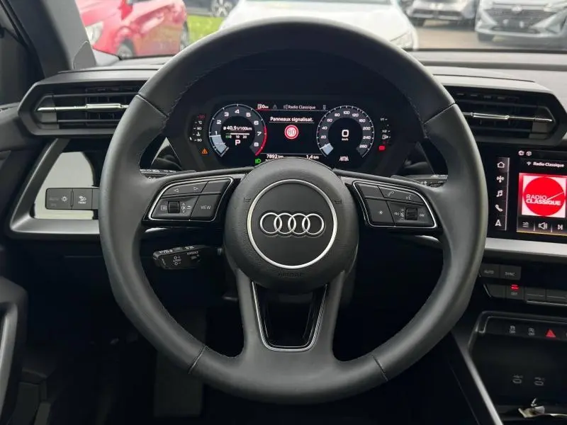 Vue frontale du volant cuir multifonction et tableau de bord numérique de l'Audi A3 Sportback 2024 hybride.