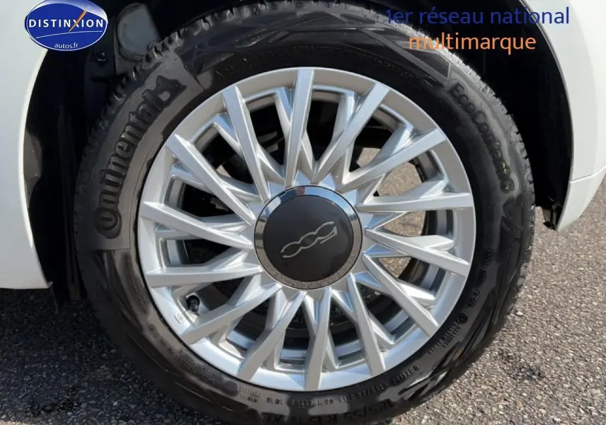 Gros plan sur la roue avant droite d'une FIAT 500 blanche avec jante alu à rayons fins et logo central noir.