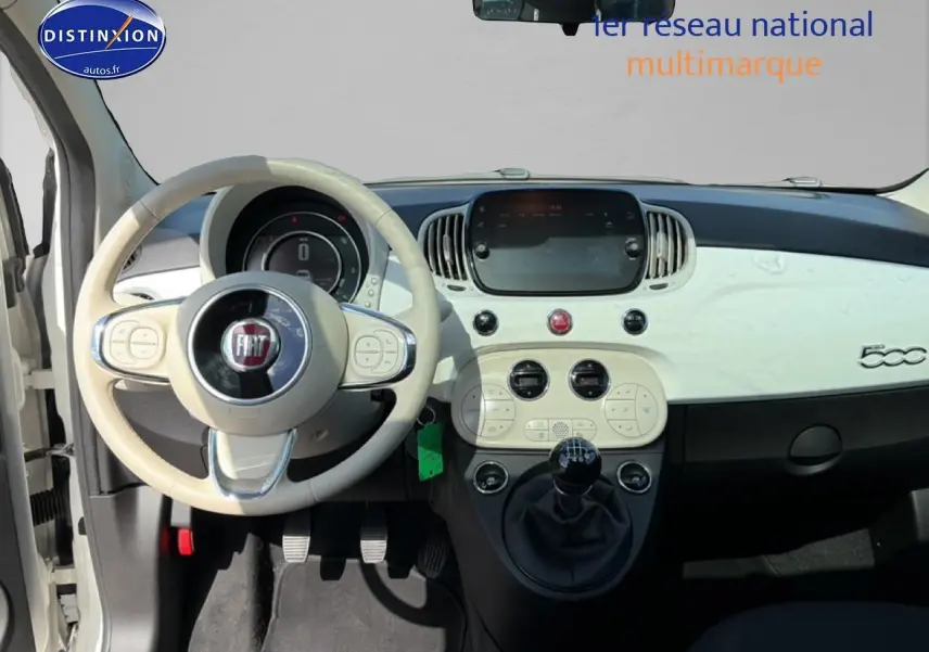 Vue intérieure avant centrée sur le tableau de bord blanc et volant beige de la Fiat 500 2023 avec boîte manuelle.