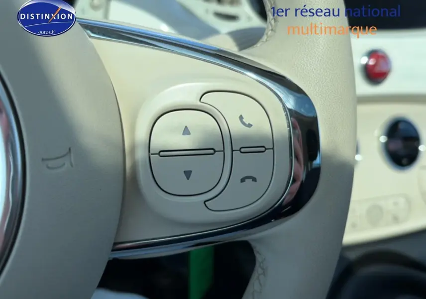 Gros plan sur les commandes du volant beige de la Fiat 500 blanche, avec boutons de gestion d'appels et volume.