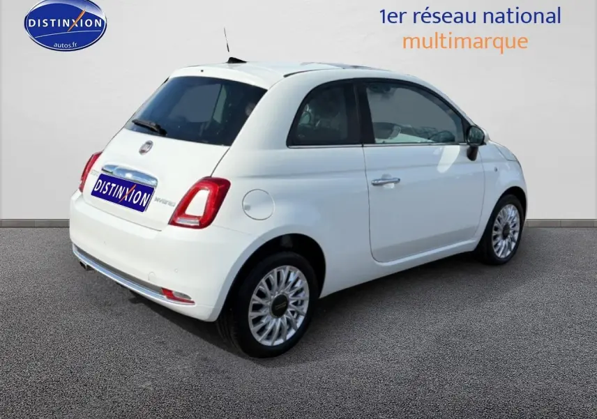 Vue 3/4 arrière droite d'une Fiat 500 blanche 2023 avec jantes alu et toit panoramique en verre.