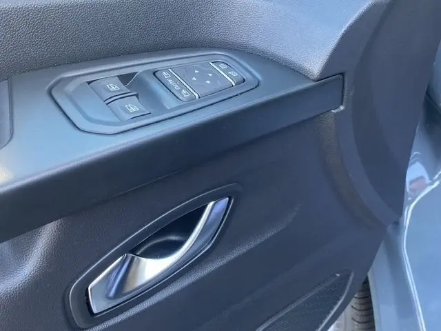 Gros plan sur la poignée intérieure et les commandes des vitres côté conducteur du Renault Trafic Fourgon gris foncé.