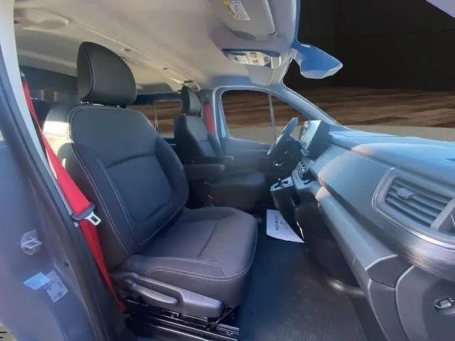 Vue intérieure côté conducteur du Renault Trafic Fourgon gris foncé, montrant les sièges avant et le tableau de bord moderne.