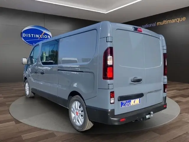 Vue 3/4 arrière droite d’un Renault Trafic Fourgon gris foncé avec feux LED et attelage visible en showroom.