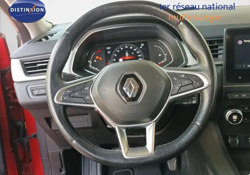 Vue intérieure centrée sur le volant noir avec logo Renault, tableau de bord digital et partie rouge de la portière visible.
