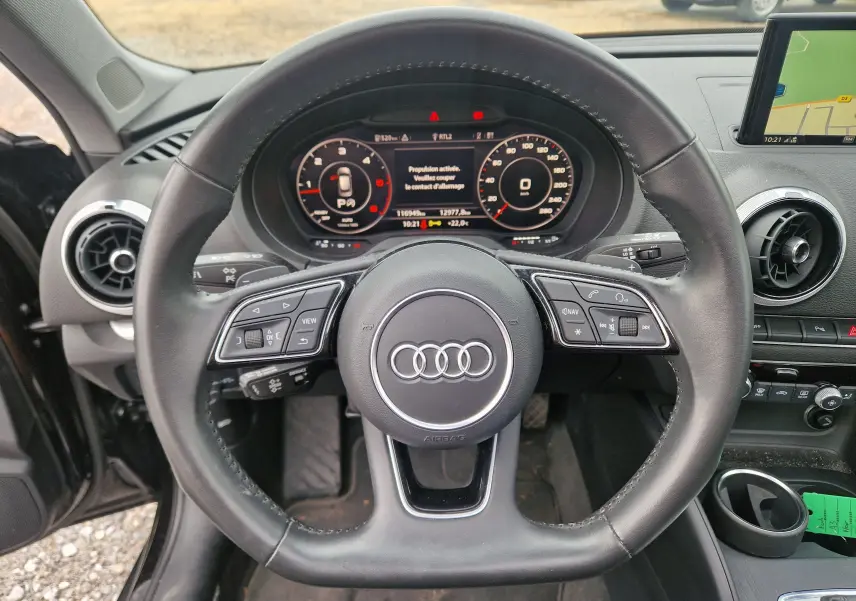 Vue rapprochée du volant en cuir noir d'une Audi A3 Sportback 35 TDI 2019 avec tableau de bord numérique et écran GPS.