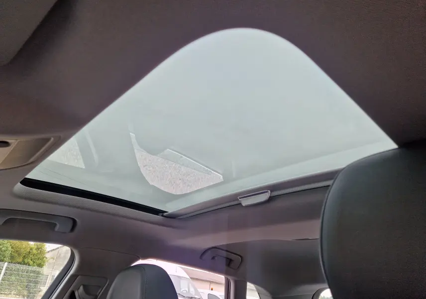 Toit panoramique ouvert vu de l'intérieur arrière d'une Audi A3 Sportback noire, sièges en cuir visibles.
