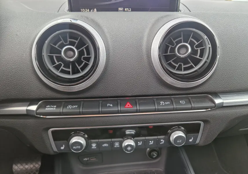 Vue rapprochée du tableau de bord noir de l'Audi A3 Sportback 2019, avec aérateurs ronds et commandes climatisation.