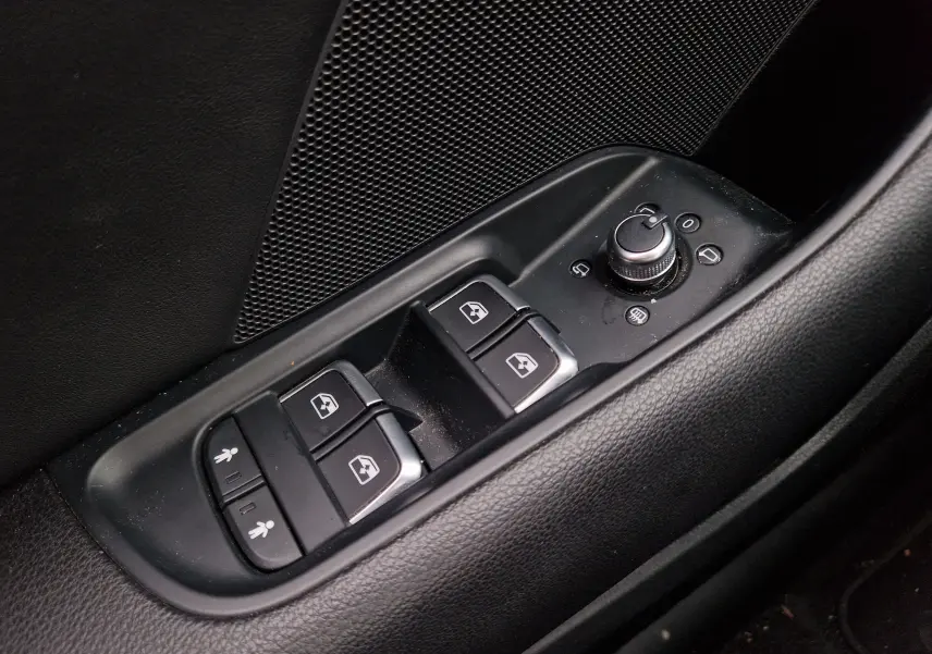 Gros plan sur les commandes de lève-vitres et réglage des rétroviseurs côté conducteur d’une Audi A3 Sportback noire.
