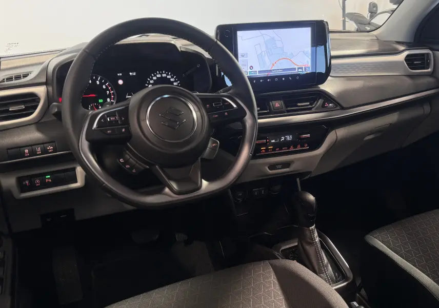Intérieur de la Suzuki Swift 2025 vue côté conducteur, tableau de bord noir avec écran tactile et volant multifonctions.