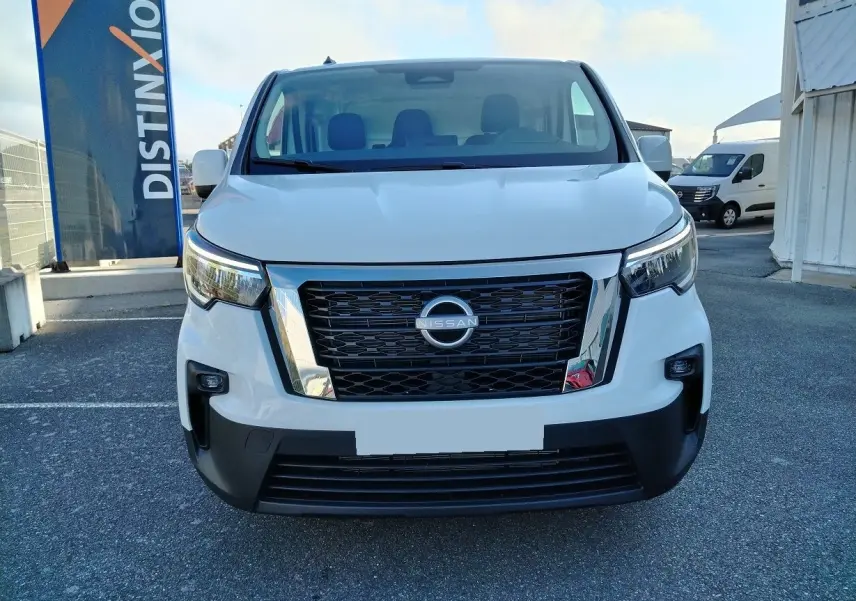 Vue de face d'un Nissan Primastar blanc 2025 avec calandre noire et détails chromés sur un parking extérieur.