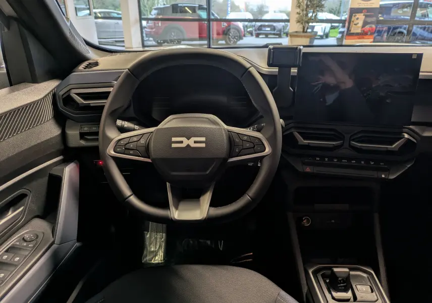 Vue intérieure centrée sur le volant multifonction et l'écran tactile du tableau de bord du Dacia Duster blanc Glacier 2025.