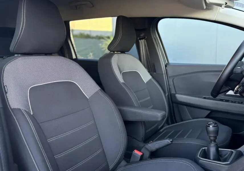 Vue intérieure côté conducteur du Dacia Jogger 2025, sièges tissu noir avec accoudoir central et levier de vitesses manuel.