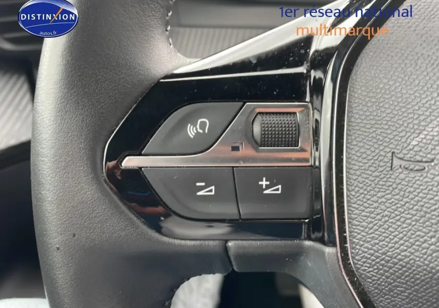 Gros plan sur les commandes gauche du volant noir du Peugeot 2008 E-136 allure gris sélénite, boutons de volume et appel mains-libres.