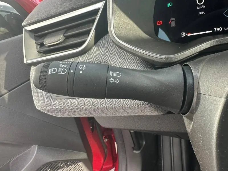 Détail intérieur du commodo des feux sur Renault Clio 2025 Rouge Flamme, avec tableau de bord numérique en arrière-plan.