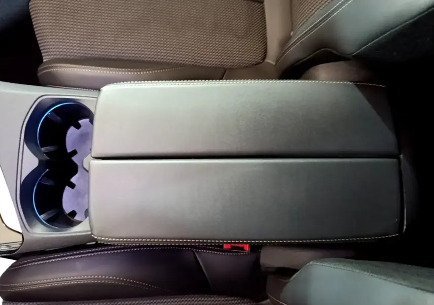 Vue plongeante sur l'accoudoir central noir et les sièges marron du Peugeot 3008 GT 2023, avec porte-gobelets éclairé.