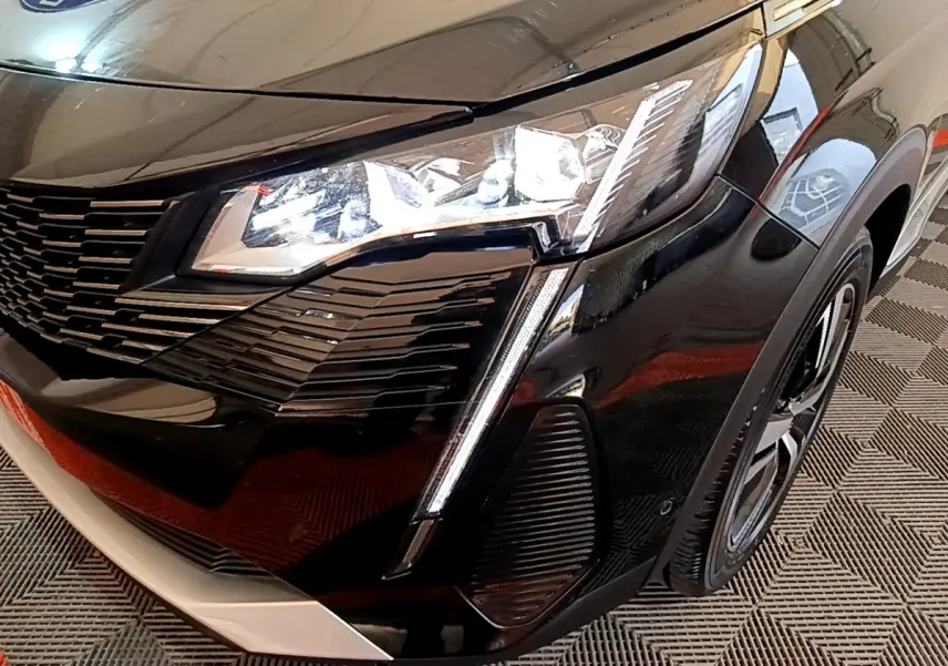 Gros plan sur l'avant droit noir brillant du Peugeot 3008 2023, mettant en valeur son phare LED et sa calandre distinctive.