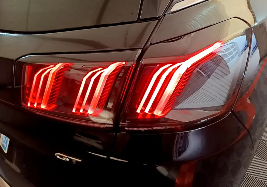 Gros plan sur les feux arrière allumés côté droit d’un Peugeot 3008 GT noir de 2023.