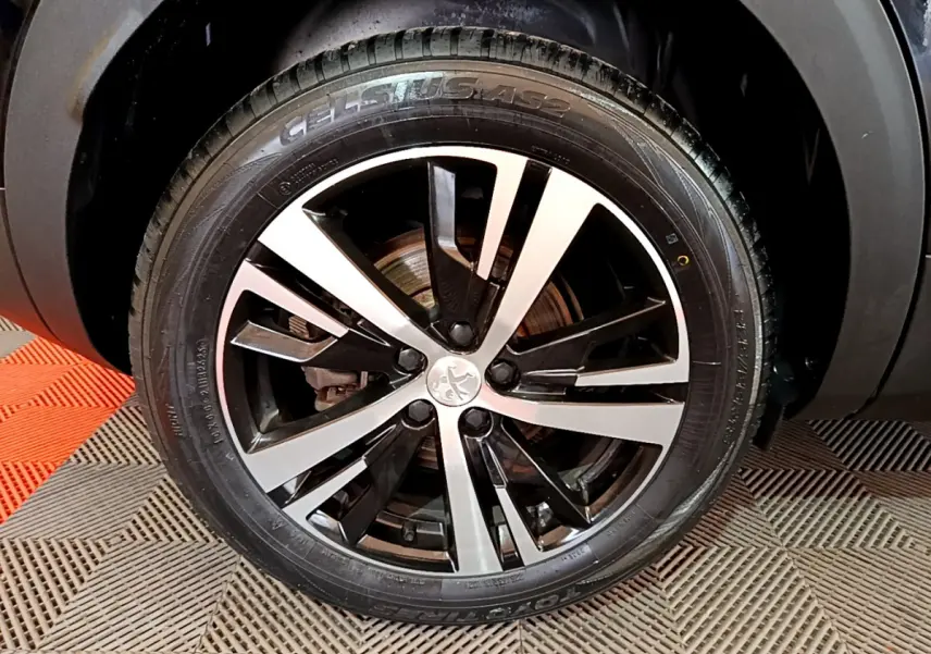 Gros plan sur la roue avant droite du Peugeot 3008 noir, mettant en valeur la jante alliage bicolore au design moderne.