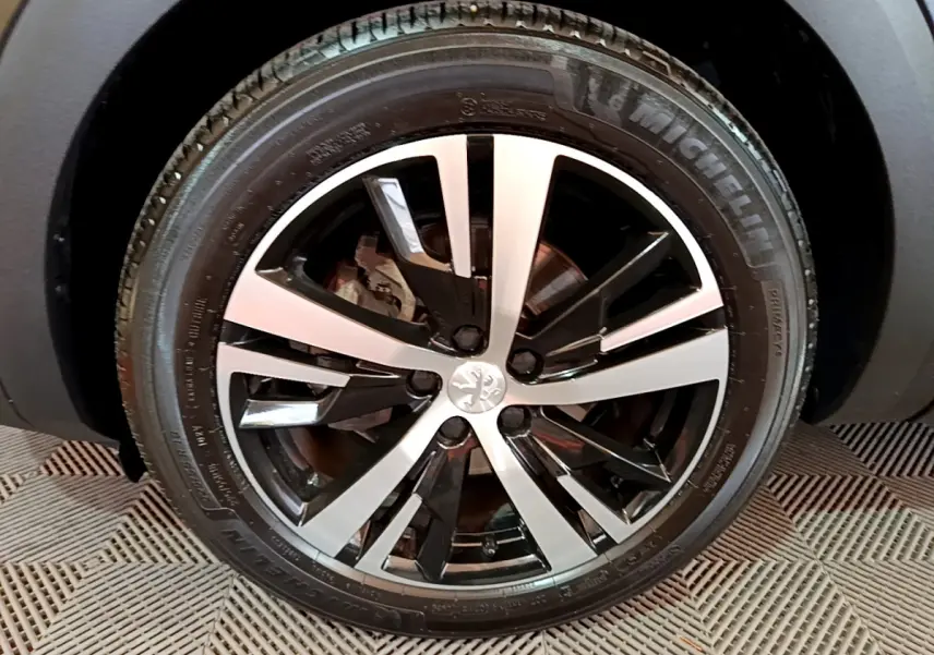 Gros plan sur la roue avant droite du Peugeot 3008 noir, mettant en valeur la jante alliage bicolore au design moderne.