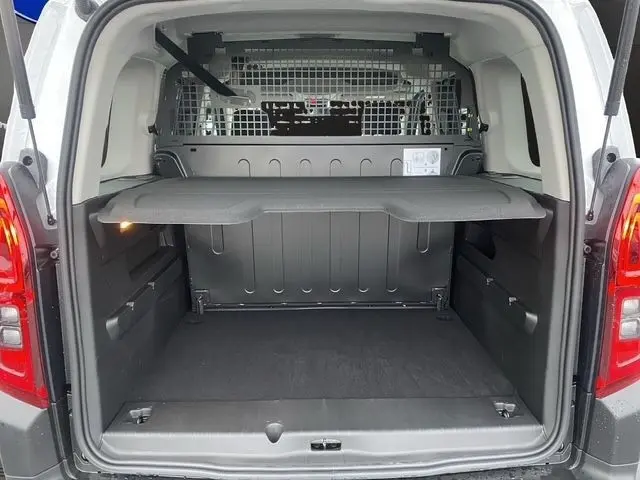 Vue arrière ouverte du coffre noir d’un Citroën Berlingo blanc 2025 avec séparation grillagée et tablette de rangement.
