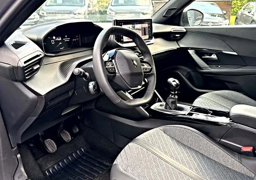 Intérieur avant droit du Peugeot 2008 1.2 100 Allure 2025, volant multifonction, boîte manuelle et sièges tissu gris.