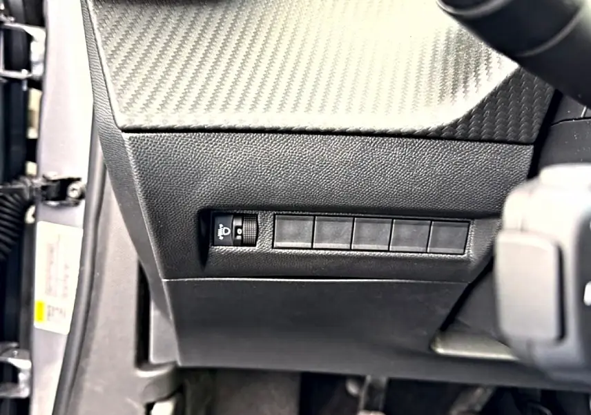 Détail intérieur côté gauche du tableau de bord noir avec commande de réglage des phares sur Peugeot 2008 gris Artense.