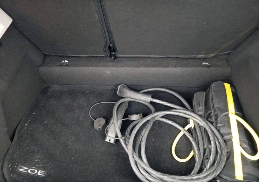 Coffre ouvert d’une Renault ZOE électrique 2022, vue intérieure montrant un câble de recharge et un sac noir avec liseré jaune.