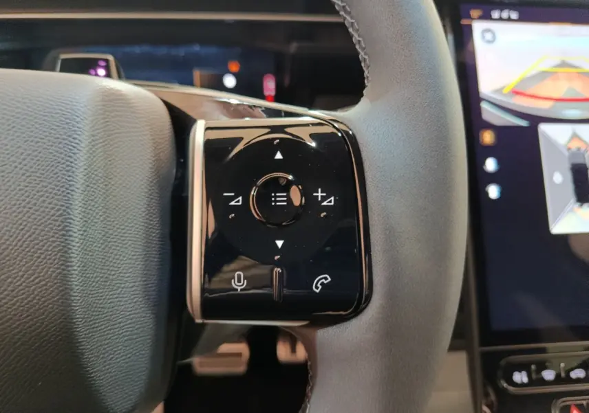 Gros plan sur les commandes multifonctions noires à gauche du volant cuir gris du Citroën C5 Hybride 2026.