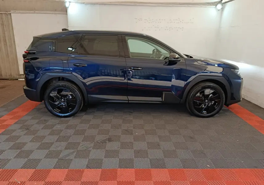 Profil côté droit d'une Citroën C5 hybride bleu foncé avec jantes noires, dans un garage éclairé.