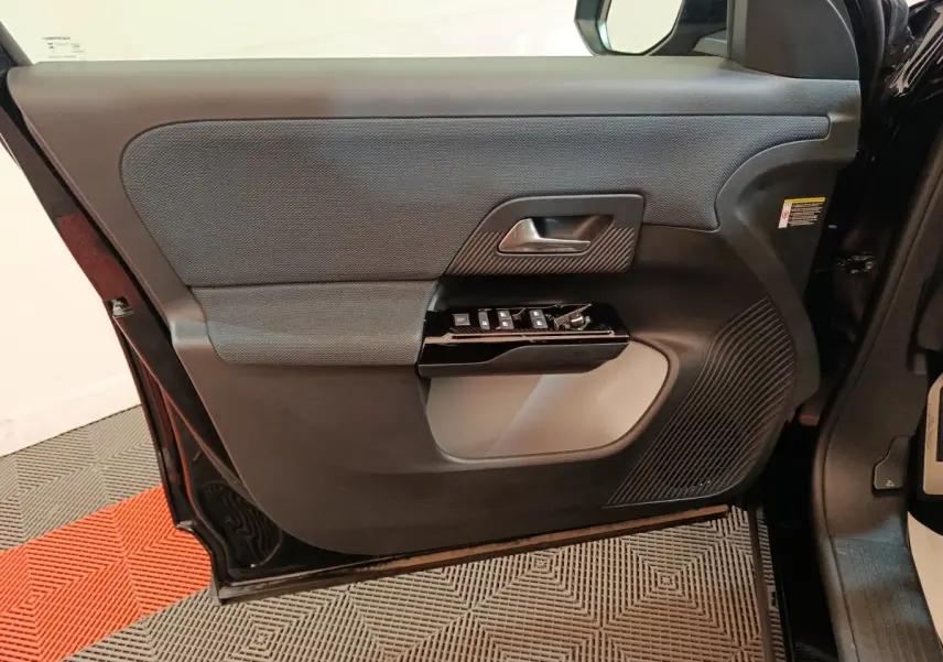 Vue intérieure côté gauche de la porte avant d’une Citroën C5 Hybride 2026 avec commandes de vitres et poignée noire.