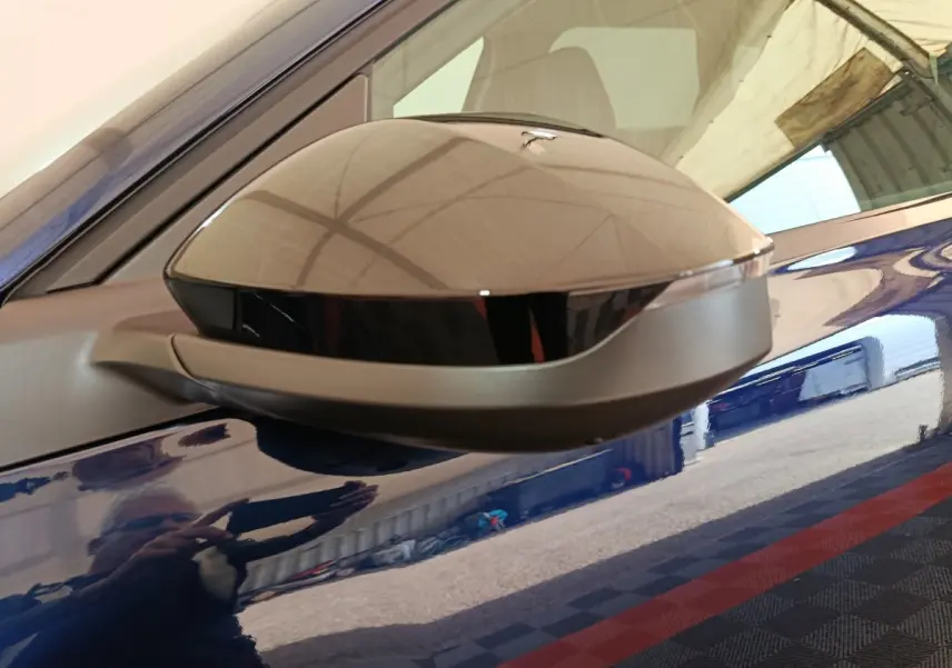 Gros plan sur le rétroviseur droit gris et noir du Citroën C5 hybride bleu, reflétant l'environnement intérieur.