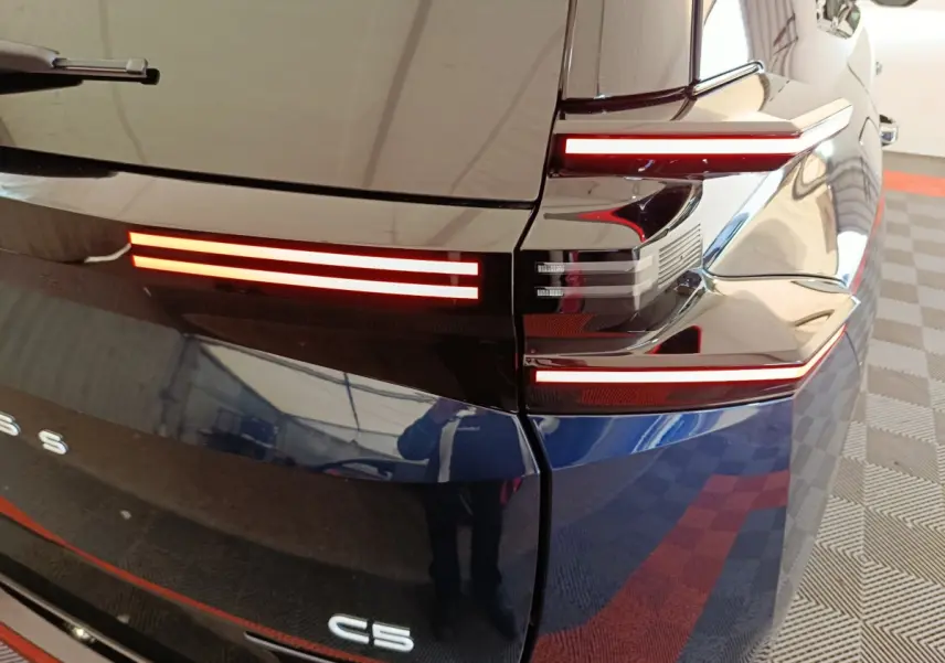 Gros plan sur l'arrière droit bleu du Citroën C5 hybride 2026, mettant en valeur les feux LED horizontaux distinctifs.