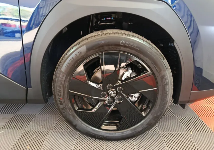 Gros plan sur la roue arrière droite noire brillante d'une Citroën C5 hybride bleu 2026 avec jante design et pneu Michelin.